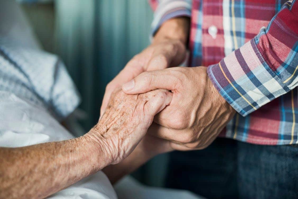 An elderly person holding hands with their caregiver.